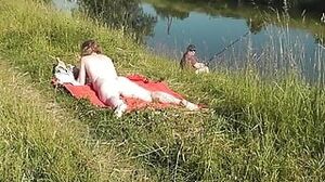 Nudist beach. Public nudity. Sexy MILF without panties and bra sunbathes naked is not shy about fisherman. Naked in public. Milf